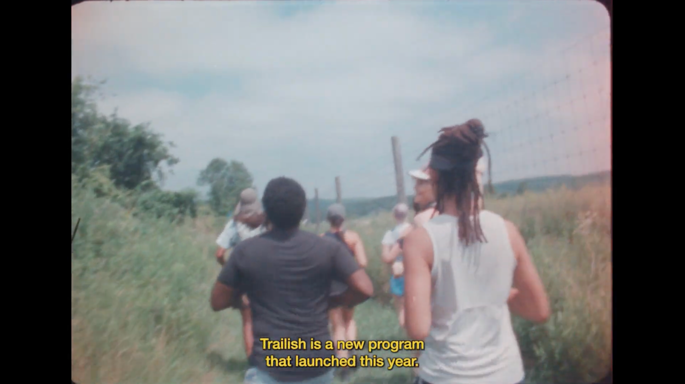 Load video: A group of runners run with a trail running club in a wooded area, shot on 16mm film and narrated by the run leader, Travis Basora, and Trailish founder, Benje Williams